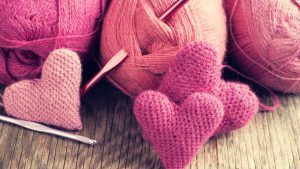 Crochet pink hearts and yarn on wooden background.